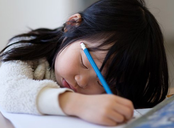 Exhausted girl with children’s sleep apnea sitting at desk